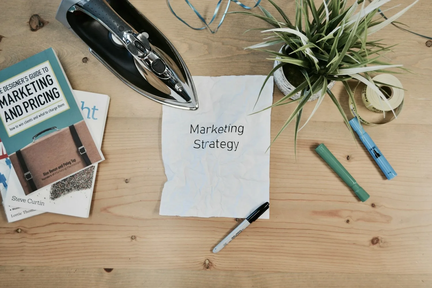 Sheet of paper titled “Marketing Strategy” on a wooden table with a pen and plant